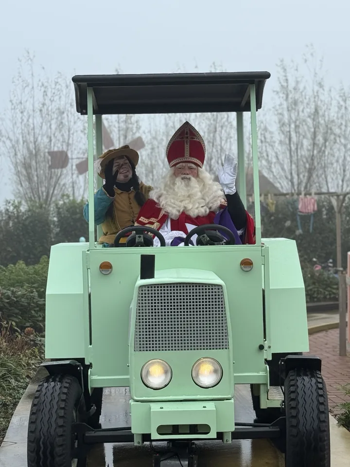 Kerstman en begeleider in een groen boerderijvoertuig